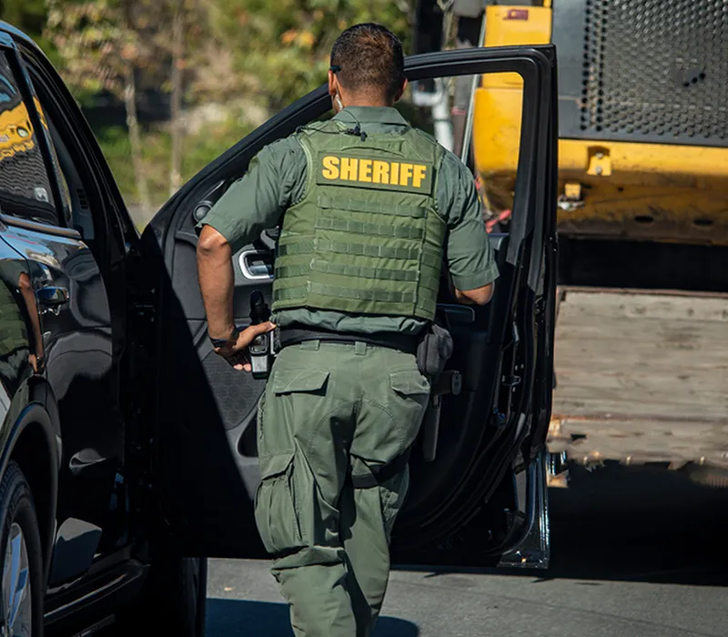 Sheriff in tactical vest opening the door of a patrol vehicle